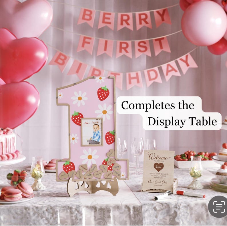 Puede incluir: Un letrero rosa con el n&uacute;mero uno con un patr&oacute;n de fresas y margaritas, con una foto. El letrero es parte de una exhibici&oacute;n de primer cumplea&ntilde;os, con una pancarta que dice "Berry First Birthday".