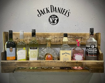 May include: A wooden wall-mounted shelf with a variety of bottles of alcohol, including Jack Daniel's Tennessee Honey, Jack Daniel's Old No. 7, and Russian Standard Vodka. The shelf is labeled with the Jack Daniel's logo.