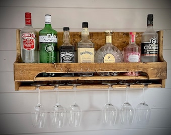 Peut inclure: Un porte-bouteilles mural en bois avec deux étagères et six supports pour verres. Le porte-bouteilles est rempli de diverses bouteilles d'alcool, notamment de la vodka Smirnoff, du gin Gordon's, du whisky Jack Daniel's Tennessee, du miel Jack Daniel's Tennessee, du cognac Remy Martin et de la vodka Russian Standard.