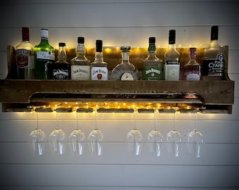 Peut inclure: Un porte-bouteilles mural en bois avec une rangée de verres à vin en verre transparent suspendus en dessous. Le porte-bouteilles est rempli de diverses bouteilles d'alcool, dont Jack Daniels, Jim Beam et Gordons Gin.