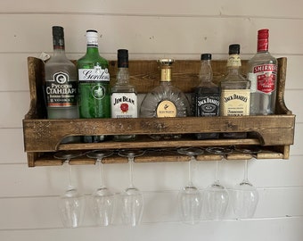 Peut inclure: Étagère de bar en bois rustique avec une sélection de bouteilles d'alcool, dont de la vodka, du gin et du whisky. L'étagère comprend également une rangée de verres à vin suspendus.