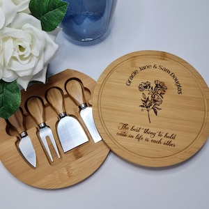 Puede incluir: Una tabla de queso redonda de madera con un diseño floral y el texto "Grace Jane & Sam Douglas" y "The best thing to hold onto in life is each other". La tabla tiene un juego a juego de cuatro cuchillos para queso.