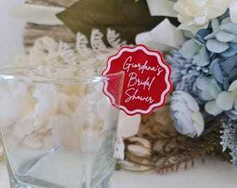 Può includere: Un adesivo rotondo rosso e bianco con bordi a festoni con il testo "Giordana's Bridal Shower" in lettere bianche.