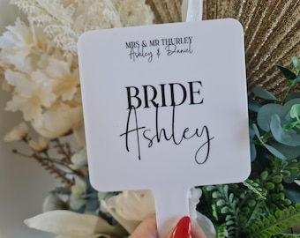 Puede incluir: Espejo de mano cuadrado blanco con un mango negro. El espejo tiene el texto "MRS & MR THURLY Ashley & Daniel" y "BRIDE Ashley" impreso en él.