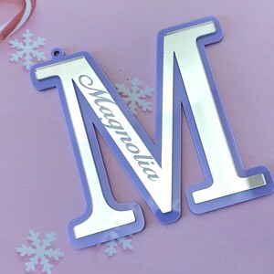 May include: A light purple acrylic letter M with a silver mirror finish. The letter is personalized with the name "Magnolia" in a cursive font.