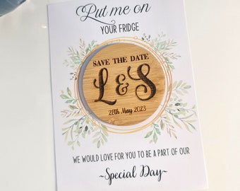 May include: A save-the-date magnet with a wooden circular insert featuring the initials "L&S" and the date "28th May 2023". The card reads "Put me on your fridge" and "Special Day". The design includes a floral wreath.
