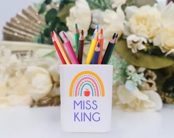 Puede incluir: Porta lápices de cerámica blanca con un diseño de arcoíris y el texto "Miss King". El arcoíris tiene una manzana roja en el centro y las palabras "Cree, Sueña, Inspira, Motiva, Enseña, Ama, Aprende, Anima".