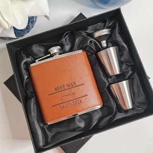 May include: A tan leather hip flask with silver trim, engraved with "BEST MAN", a name and date, in a black gift box with two shot glasses and a funnel. A traditional gift for a wedding.