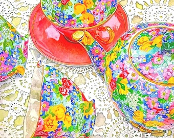 May include: A colorful floral tea set featuring a teapot, teacup, and saucer. The teacup and teapot are adorned with a vibrant pattern of flowers in shades of pink, yellow, blue, and green. The saucer is a solid red color. The set is arranged on a white lace tablecloth.