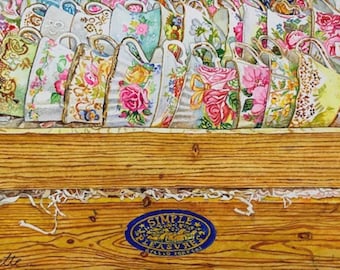 May include: A wooden box filled with vintage teacups with floral patterns. The box has a blue label that reads "Simple Pleasure" with a small floral design.