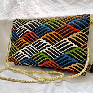 Può includere: Una borsa in tessuto nero con un motivo geometrico colorato di onde. La borsa ha una lunga tracolla in corda color crema con un fiocco.