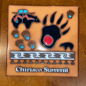 May include: Square ceramic tile with a brown background featuring a black bear, bear paw prints, and the text "Chiriaco Summit." The bear paw prints have red and blue accents. The tile has a decorative border.