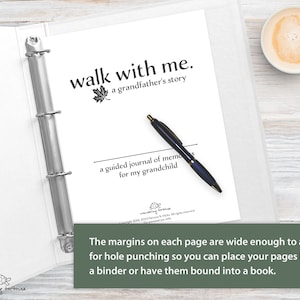Op de afbeelding: Een wit dagboek met een zwarte binder, een pen en de tekst "walk with me. a grandfather's story" en "a guided journal of memories for my grandchild". De marges op elke pagina zijn breed genoeg om te kunnen perforeren, zodat je je pagina's in een map kunt plaatsen of kunt laten binden tot een boek.