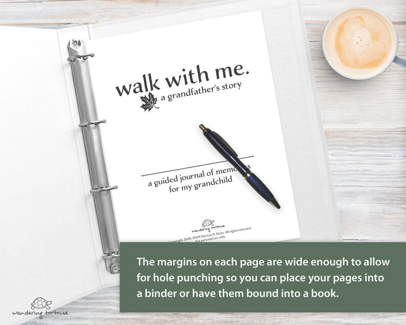 Op de afbeelding: Een wit dagboek met een zwarte binder, een pen en de tekst "walk with me. a grandfather's story" en "a guided journal of memories for my grandchild". De marges op elke pagina zijn breed genoeg om te kunnen perforeren, zodat je je pagina's in een map kunt plaatsen of kunt laten binden tot een boek.