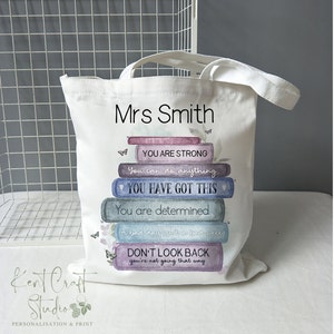 May include: A white canvas tote bag with the text "Mrs Smith" printed on the front. The bag features a stack of books with inspirational quotes, including "You are strong", "You can do anything", "You have got this", "You are determined", "A bad day isn't a bad week", and "Don't look back, you're not going that way".