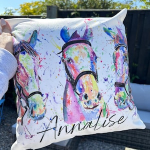 May include: White pillow with a watercolor painting of three horses' heads. The horses are painted in shades of pink, blue, green, and yellow. The pillow is personalized with the name "Annalese" in black cursive.