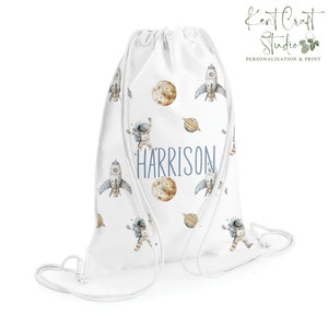 May include: White drawstring bag with a space theme. The bag features a repeating pattern of astronauts, rockets, planets, and stars. The name "HARRISON" is printed in blue on the bag.
