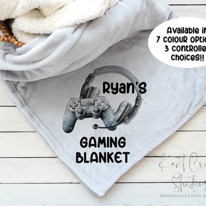 May include: A grey fleece blanket with a personalised gaming design. The design features a grey video game controller with headphones, the text "Ryan's" and the words "Gaming Blanket".