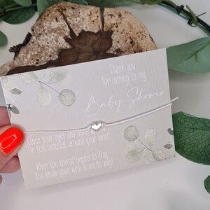 May include: White string bracelet with a silver heart charm and a card that says "Thank you for coming to my Baby Shower. Close your eyes and make a wish. Tie this bracelet around your wrist. When the thread begins to fray, you know your wish is on its way!"