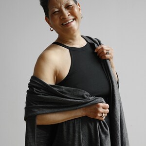 May include: A woman with short dark hair is wearing a black sleeveless top and a gray shawl. She is smiling and looking at the camera.