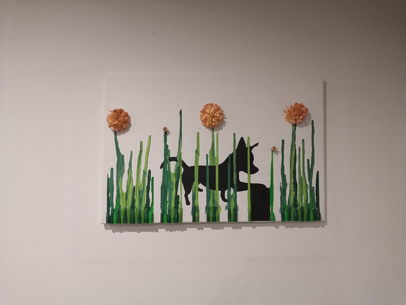 May include: A black silhouette of a dog standing in a field of green grass with three orange flowers on top.