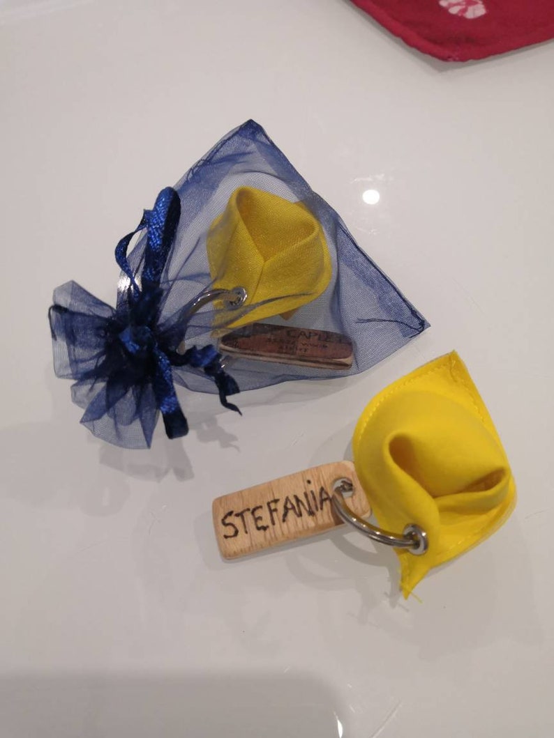 K&ouml;nnte beinhalten: Zwei gelbe Gl&uuml;ckskeks-Schl&uuml;sselanh&auml;nger aus Stoff mit Holzetiketten. Ein Etikett lautet "Stefania" und das andere "Capri, Italien".