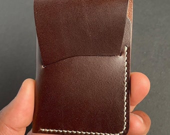 May include: A brown leather wallet with a flap closure and white stitching. The wallet is held in a hand.