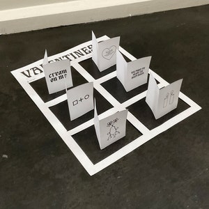 Puede incluir: Un juego de mesa blanco con una cuadrícula negra y cuadrados blancos. Los cuadrados contienen diferentes frases y dibujos, incluyendo "cream on me?", "you make my heart go boom boom", y un dibujo de un árbol. El juego de mesa se titula "Valentines".
