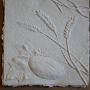 May include: A white paper relief sculpture of wheat stalks and leaves. The sculpture is made with a textured paper that gives it a three-dimensional look.