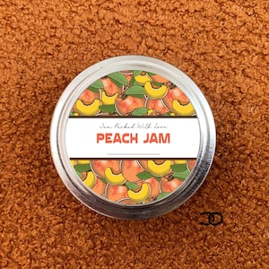 May include: A silver jar with a peach jam label. The label features a peach design and the text "Jam Packed With Love Peach Jam".