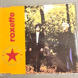 May include: CD case for the Roxette album "Fading Like a Flower". The cover features two people standing in front of a blurred forest background. The album title is in red on a yellow background, with a red star and text.