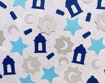 May include: A collection of paper cutouts in various shapes, including stars, crescent moons, lanterns, and small rectangular shapes. The color palette includes shades of blue and silver glitter, creating a festive and celebratory theme.