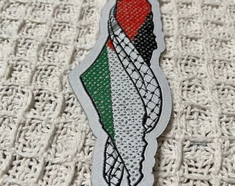 May include: An embroidered patch in the shape of Palestine with the Palestinian flag colors: green, white, black, and red.