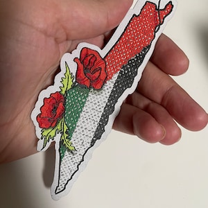 May include: An embroidered patch in the shape of Palestine with the Palestinian flag colors and red poppies.
