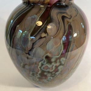 Pu&ograve; includere: Un vaso di vetro marrone con un motivo a spirale di viola, marrone e bianco. Il vaso ha un corpo rotondo e un'ampia apertura.
