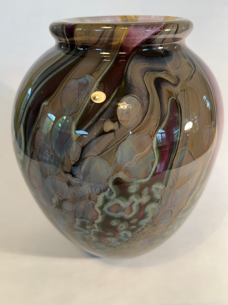 Pu&ograve; includere: Un vaso di vetro marrone con un motivo a spirale di viola, marrone e bianco. Il vaso ha un corpo rotondo e un'ampia apertura.