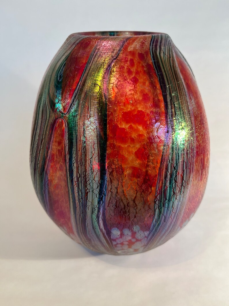 May include: A red, green, and iridescent glass vase with a textured surface. The vase has a rounded, egg-like shape.