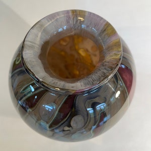Pu&ograve; includere: Un vaso rotondo in vetro con un motivo a spirale di marrone, grigio e viola. Il vaso ha un'ampia apertura e una finitura liscia e lucida.
