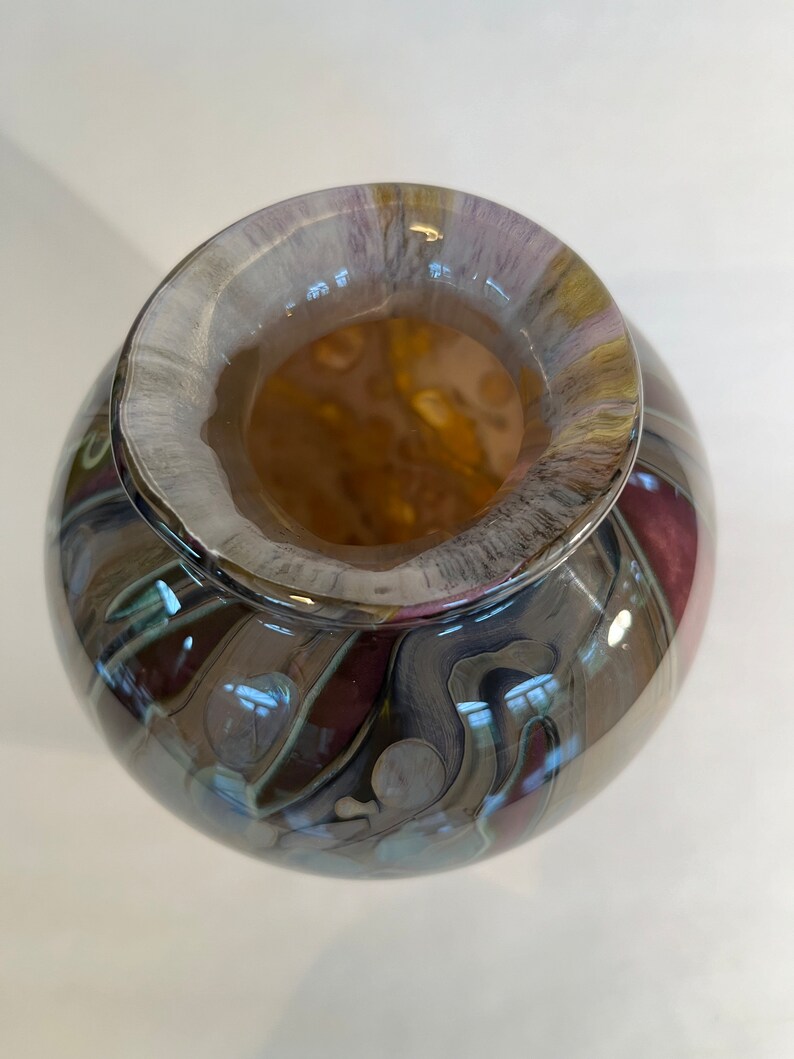 Pu&ograve; includere: Un vaso rotondo in vetro con un motivo a spirale di marrone, grigio e viola. Il vaso ha un'ampia apertura e una finitura liscia e lucida.