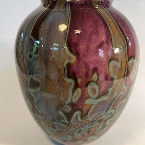 Pu&ograve; includere: Un vaso rotondo in vetro con un design marmoreo marrone, viola e verde.