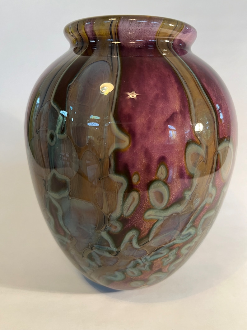 Pu&ograve; includere: Un vaso rotondo in vetro con un design marmoreo marrone, viola e verde.