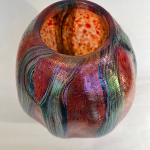 May include: A small, iridescent glass vase with a textured surface and a red, orange, and green color scheme.