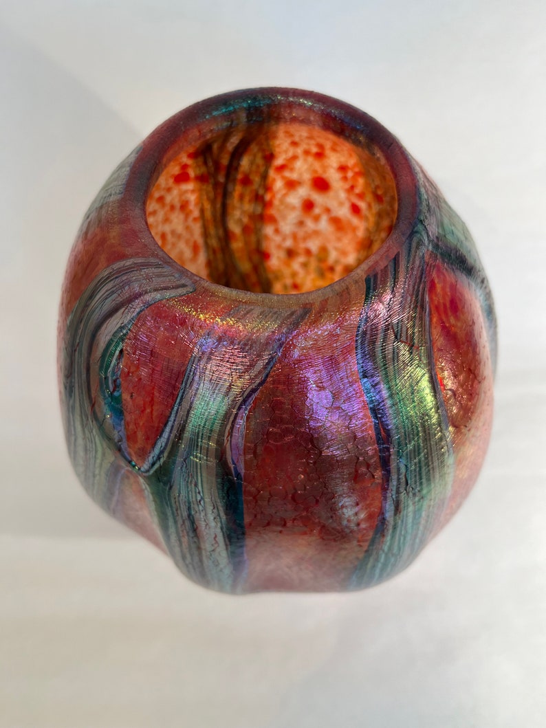 May include: A small, iridescent glass vase with a textured surface and a red, orange, and green color scheme.