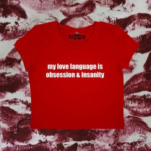 May include: Red cropped t-shirt with white text that reads "my love language is obsession & insanity".