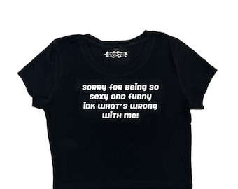 Könnte beinhalten: Schwarzes, bauchfreies T-Shirt mit weißem Text, der "Sorry for being so sexy and funny idk what's wrong with me!" lautet.