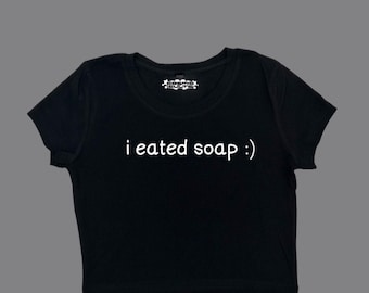 Può includere: Maglietta nera a maniche corte e crop top con il testo "i ate soap :)" in bianco.