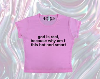 May include: A pink crop top with the text "god is real, because why am i this hot and smart" in black. The shirt has short sleeves and a crew neck. The top is made of a soft material.