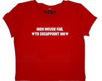 May include: Red cropped t-shirt with white text that reads "Men never fail to disappoint me" with a heart symbol on either side of the text.