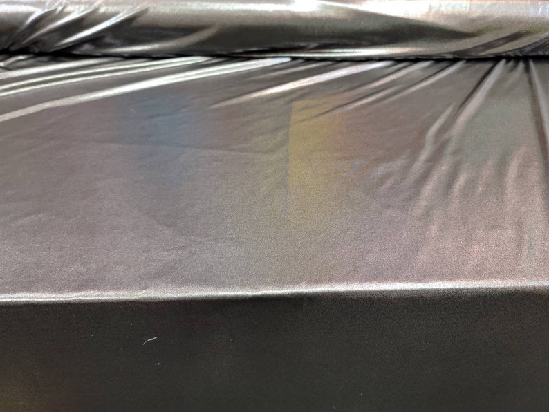 May include: A close-up of iridescent black fabric with a subtle rainbow sheen. The fabric is smooth and has a slight sheen.