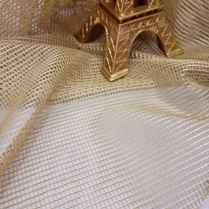 May include: A gold-colored Eiffel Tower replica figurine on a beige mesh fabric background.